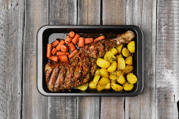 Overhead view of baked in oven lamb shoulder with potato and carrot in oven-tray