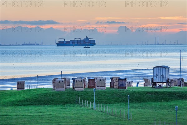 Grassy beach with beach chairs and container ship on the Weser at dusk