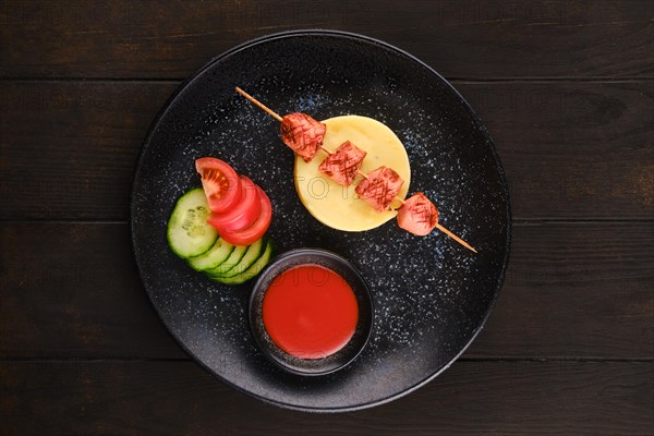 Fried sausage on skewer with mashed potato and slices of fresh tomato and cucumber