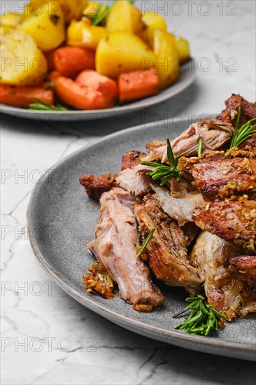 Closeup view of pulled lamb shoulder meat baked in oven with potato and carrot on marble table