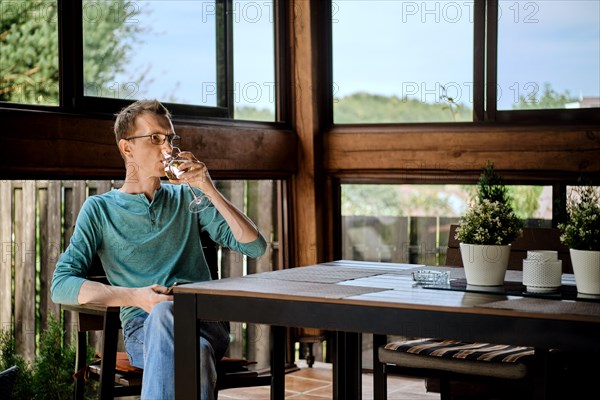 Middle aged man drinks wine sitting on the veranda of his country house