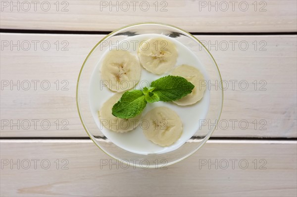 Top view of glass with yogurt and raw honey topped with sliced bananas and mint leaf. Selective focus photo