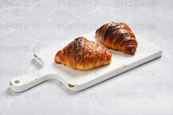 Crispy croissant on wooden serving board on marble background