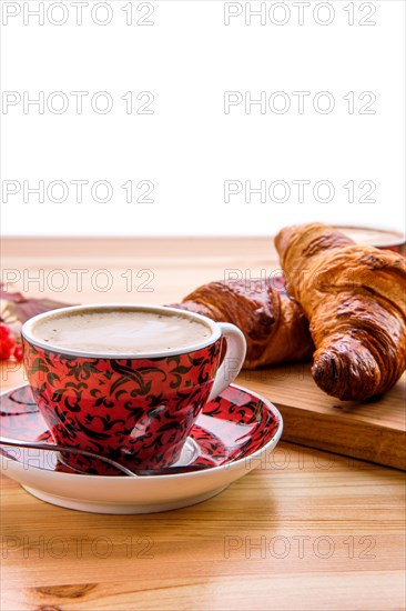 Puff pastry raisin bun and crispy croissant on wooden table with coffee