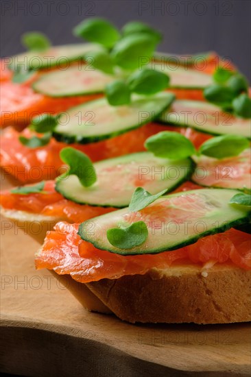 Sandwich with salmon on wooden plate on dark wooden table