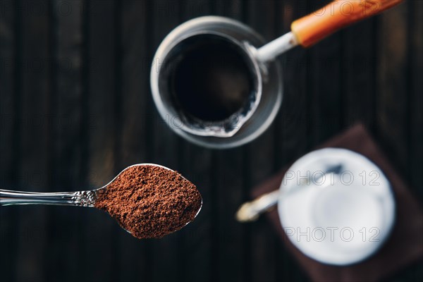 Overhead view of spoon with coffee with cezve and porcelain cup on background