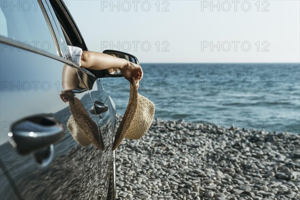 Mid shot woman hand hanging out car window holding hat near sea