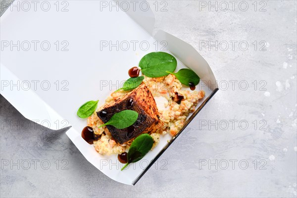 Fried salmon steak served with bulgur and sweet potato in take away cardboard package