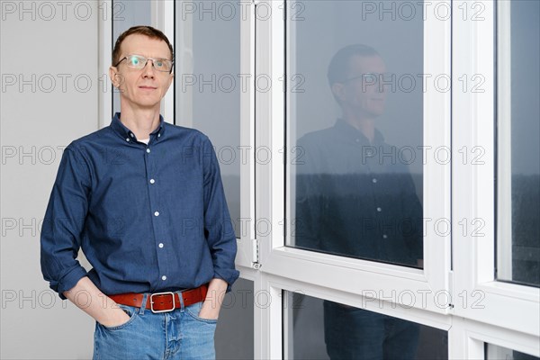 Middle-aged man is standing with hands in pockets on balcony in the early morning