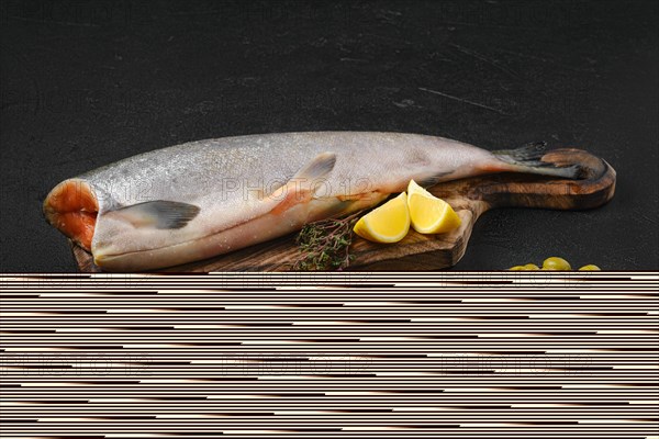 Headless fresh chinook on wooden cutting board with spice and lemon