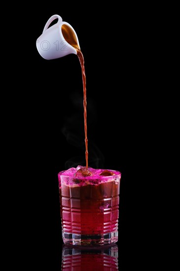 Pouring hot espresso in glass with tonic and dragon fruit syrup isolated on black background