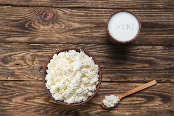 Fresh cottage cheese in clay bowl with wooden spoon with a glass of milk on rustic wooden background