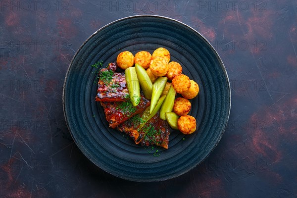 Top view of grilled ribs with pickled cucumber and fried potato balls