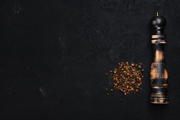 Old used wooden pepper mill with ground pepper on dark background