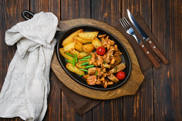 Top view of potato wedges with chanterelles and pork in cast iron skillet