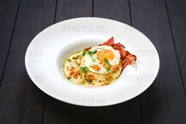 Fried egg with bacon slices and chips served with creamy sauce