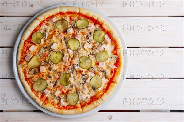 Top view of pizza with ham and pickled cucumber