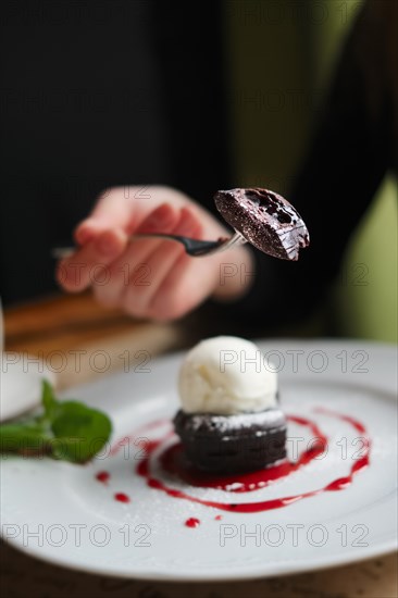 Shallow depth of foeld photo of brownie cake with ice-cream. Hand of girl with fork