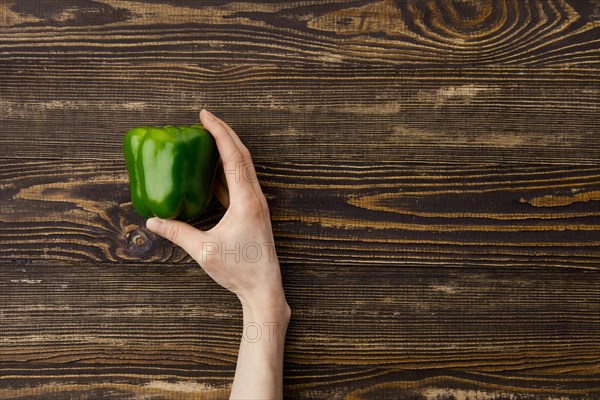 Overhead view of fresh green bell pepper in hands over wooden background