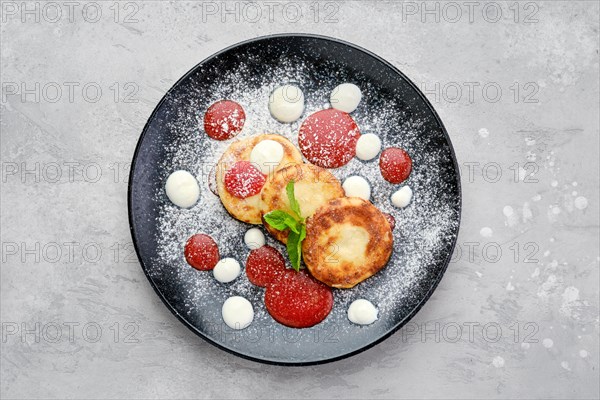 Top view of sweet curd patties with sour cream and strawberry jam on a plate