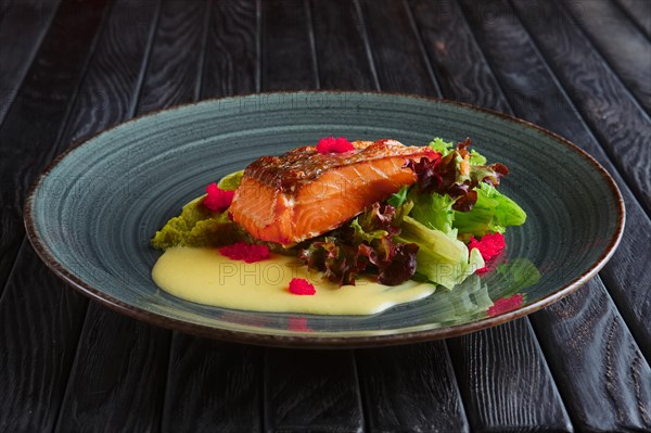 Fried salmon fillet with salad leaves and cream sauce decorated with caviar