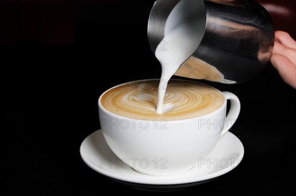 Pouring cream to cappuccino. Big white cup on black background