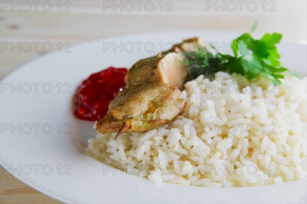 Close up view of plate with pork shaslyk with rice and tomato sauce on wooden table