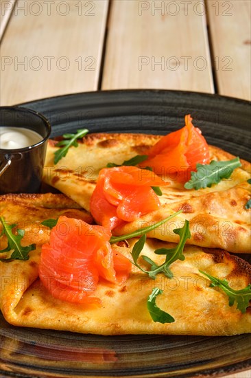 Close up view of thin pancakes with salmon and sour cream