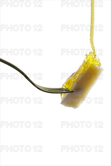 Piece of cheese on fork with floating honey