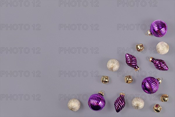 Christmas flat lay with purple and white tree ornament baubles and golden bells in corner of gray background with empty copy space