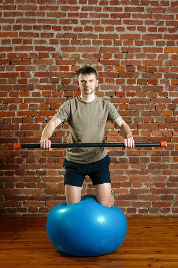 Athletic man doing exercises for the balance on rubber ball with gymnastic stick. Fitness workout