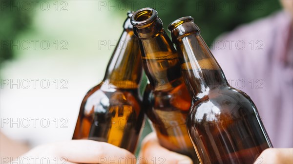 Close up friends clinking brown beer bottles