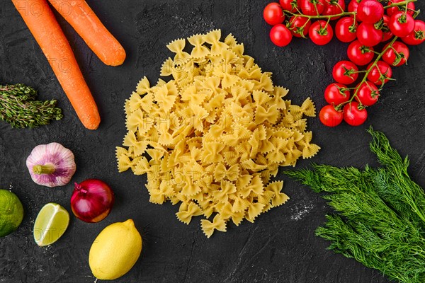 Overhead view of raw farfalle pasta with spice and herbs on black background