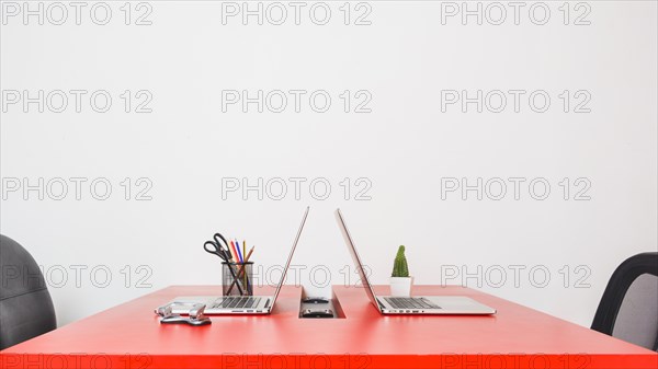 Modern workplace with two laptops red table against white wall
