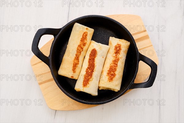 Top view of thin pancakes stuffed with turkey meat in cast iron skillet