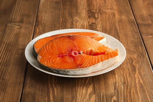 Two pieces of fresh salmom steak on a plate on wooden table