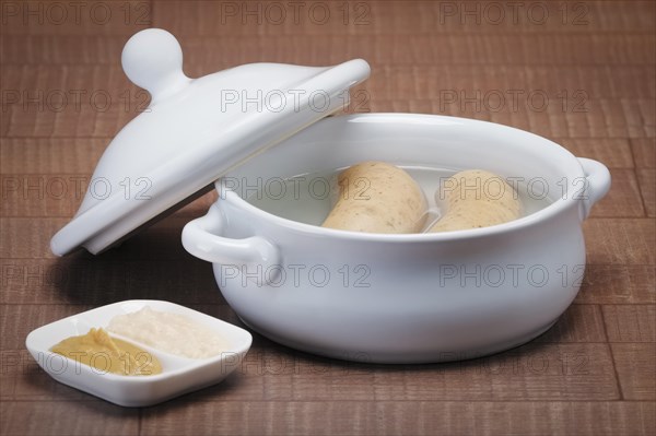 Pot with homemade sausage in broth served with mustard and horseradish