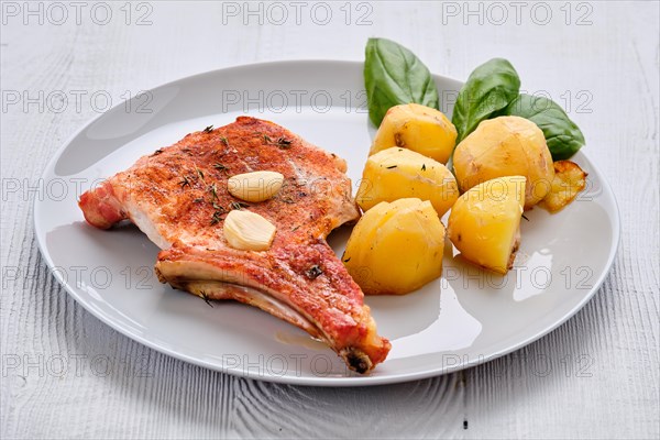 Steak with bone and potato baked in oven in a roasting pan with garlic and thyme