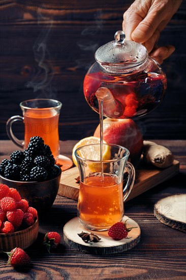 Pouring freshly brewed fruit and herbal tea from kettle into cup