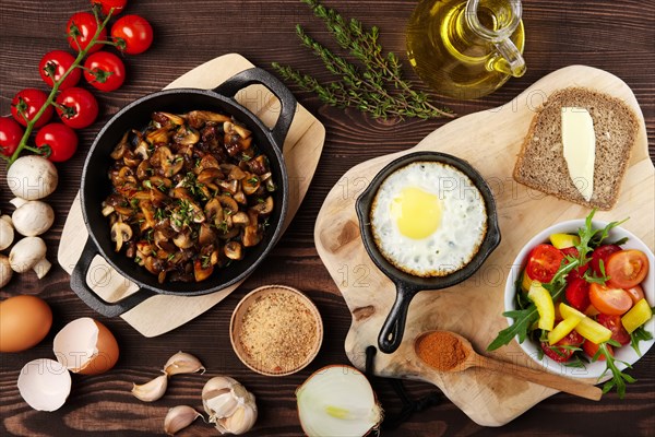 Vegetarian food. Fried mushrooms and egg in cast iron pan. Ingredients for rustic breakfast on wooden table