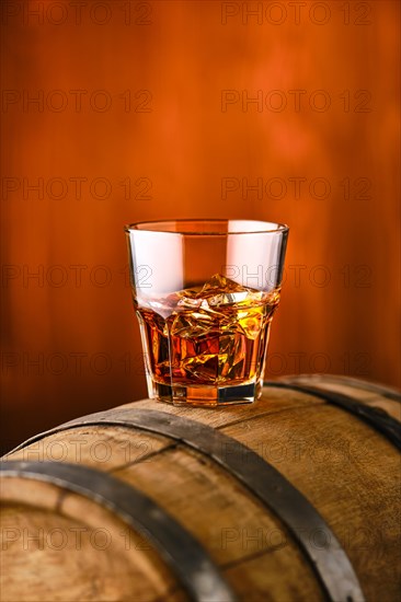 Glass of whisky with ice on the top of barrel