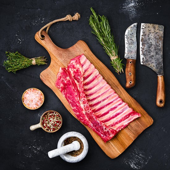 Fresh raw rack of lamb on wooden cutting board with herbs and seasoning