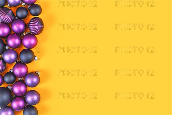 Dark purple Christmas tree bauble ornaments on side of yellow background with empty copy space