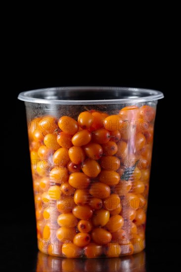 Plastic glass full of sea buckthorn on black background