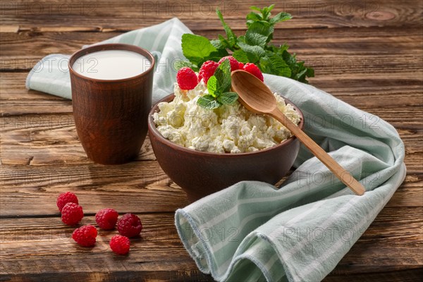 Cottage cheese with wooden spoon on it and milk in clayware on wooden table