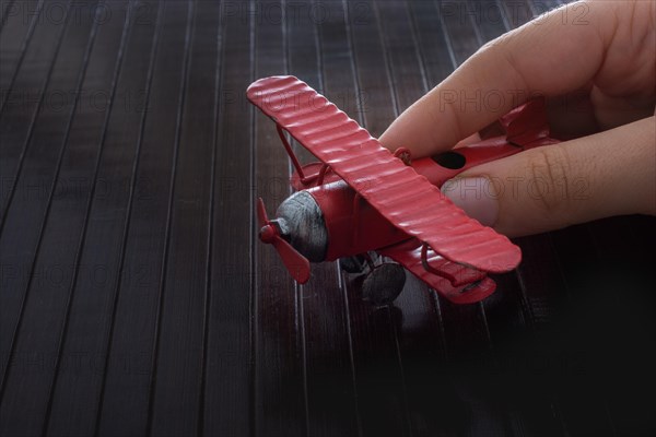 Hand holding a red toy plane on a on wooden texture