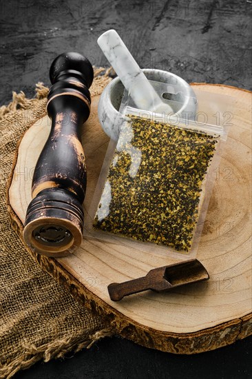 Wooden cross section with lemon pepper in plastic package and stone mortar and mill