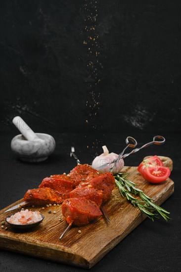 Sprinkling with spice rub raw pork meat on skewer on dark background