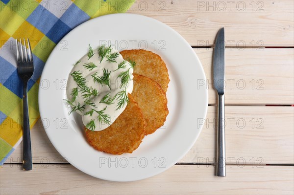 Draniki with sour cream on wooden table