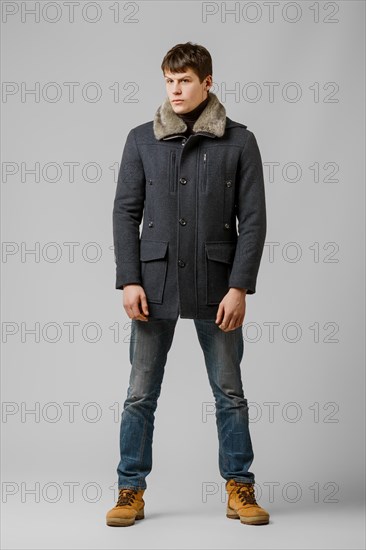 Full length portrait of handsome man in warm winter coat posing in studio